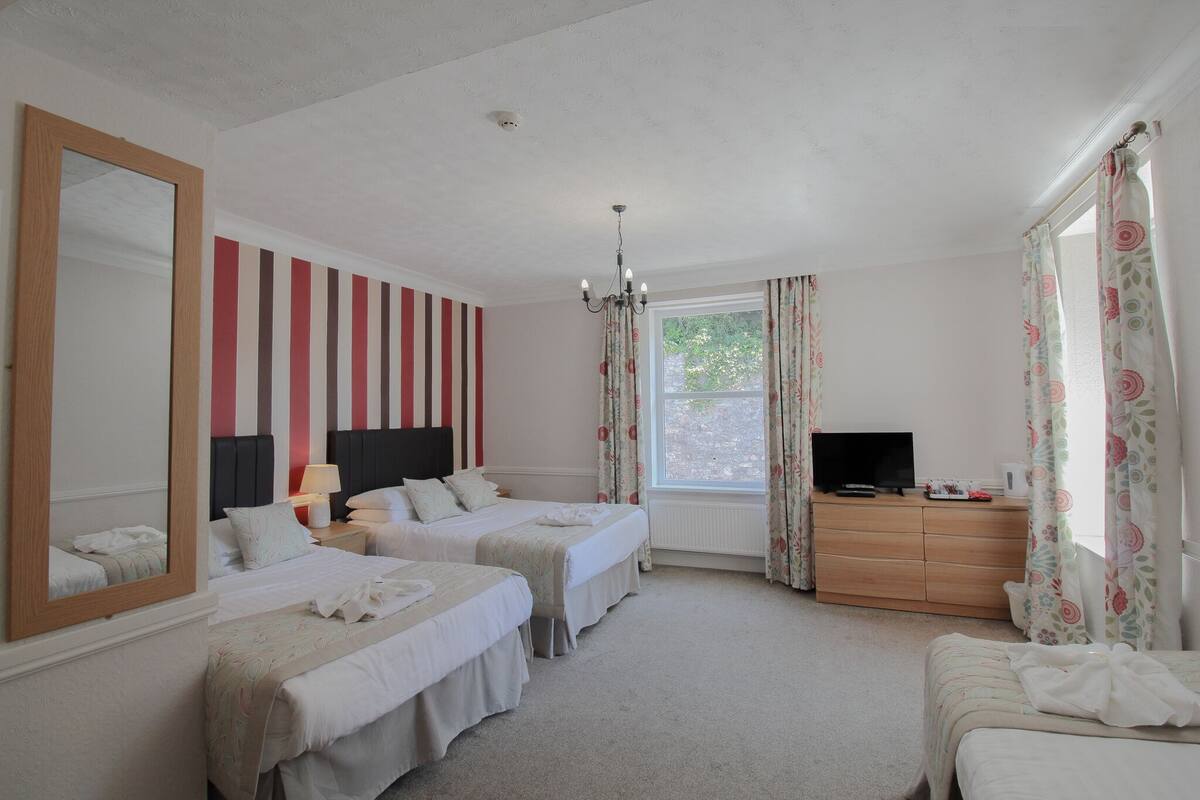 A hotel room with two beds, a large mirror, a dresser with a TV, and a window with curtains.
