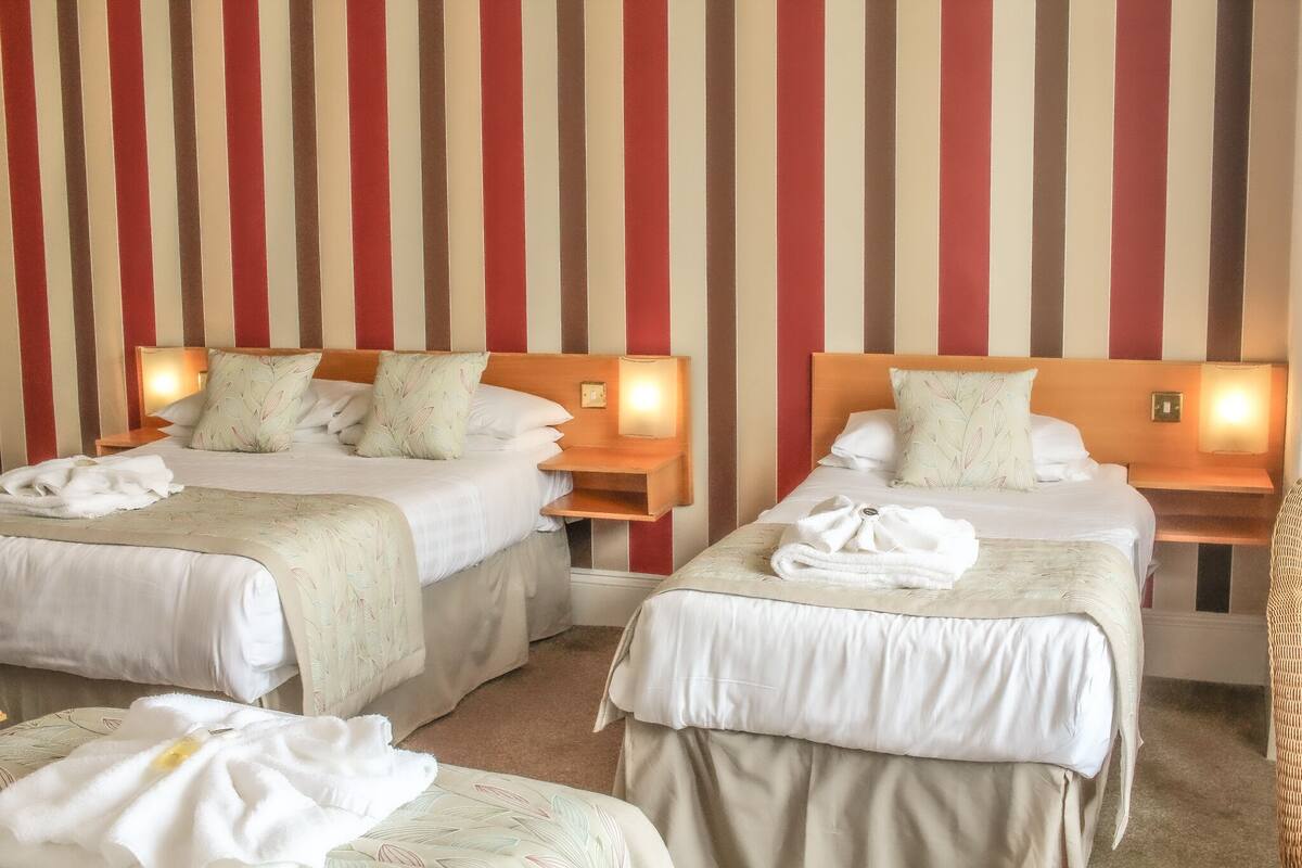 A hotel room with two beds, each with a wooden headboard, bedside tables, and lamps.