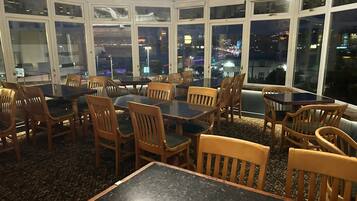 Un restaurant doté de nombreuses tables et chaises, avec de grandes fenêtres offrant une vue sur la ville la nuit.