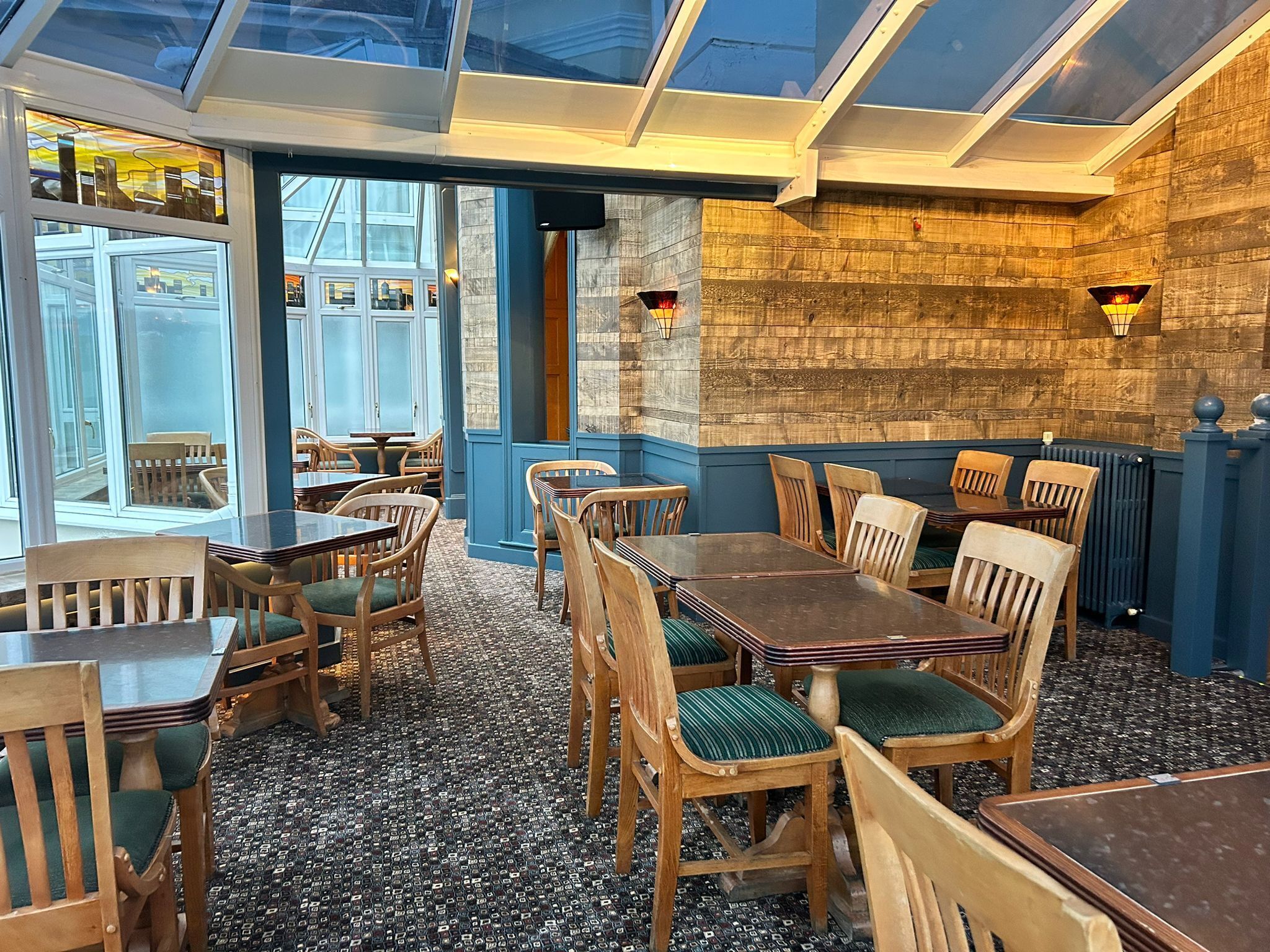 L’intérieur d’un restaurant avec des tables et des chaises en bois, un sol à motifs et une vue dégagée sur l’extérieur grâce à de grandes fenêtres.
