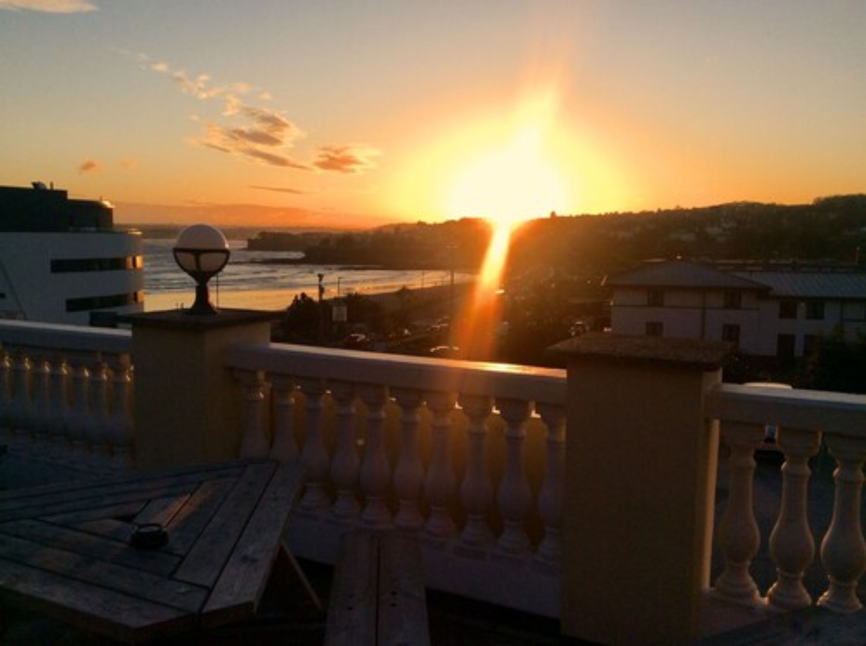A sunset view from a balcony overlooking a river with buildings in the distance.