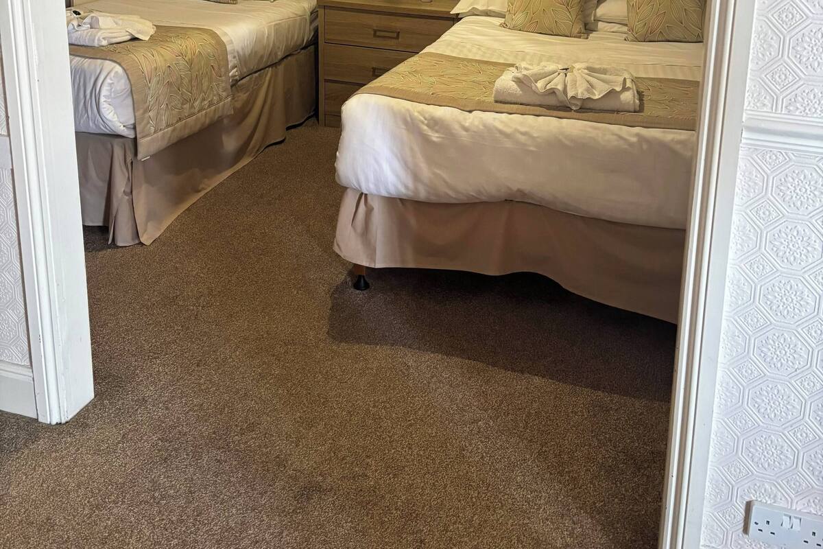 A hotel room with two beds, a nightstand, a lamp, and a patterned wall.