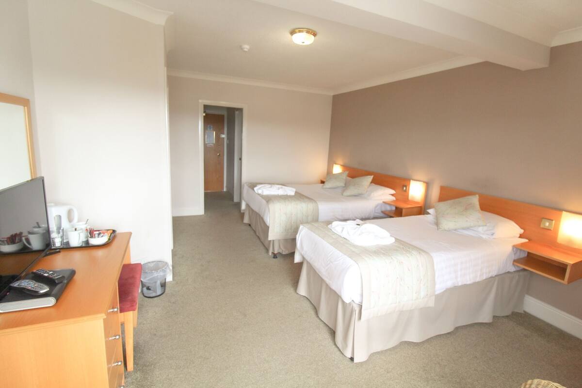 A hotel room with two beds, a desk with a computer and a telephone, and a mirror.