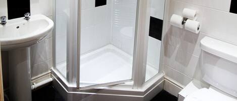 Un baño con ducha envuelta en vidrio, lavamanos e inodoro.