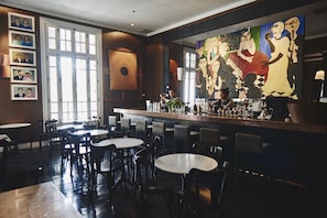 A bar area with multiple tables and chairs, a large painting on the wall, and framed pictures on the left.