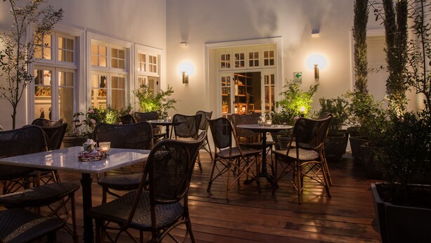 An outdoor patio with tables and chairs, surrounded by potted plants and illuminated by wall sconces. - Hotel B (Lima)