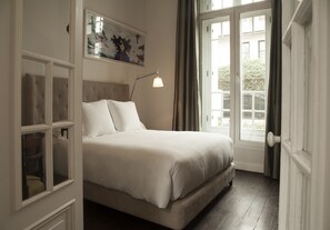 A bedroom with a bed, a nightstand, a lamp, a window with curtains, and a door. - Hotel B (Lima)