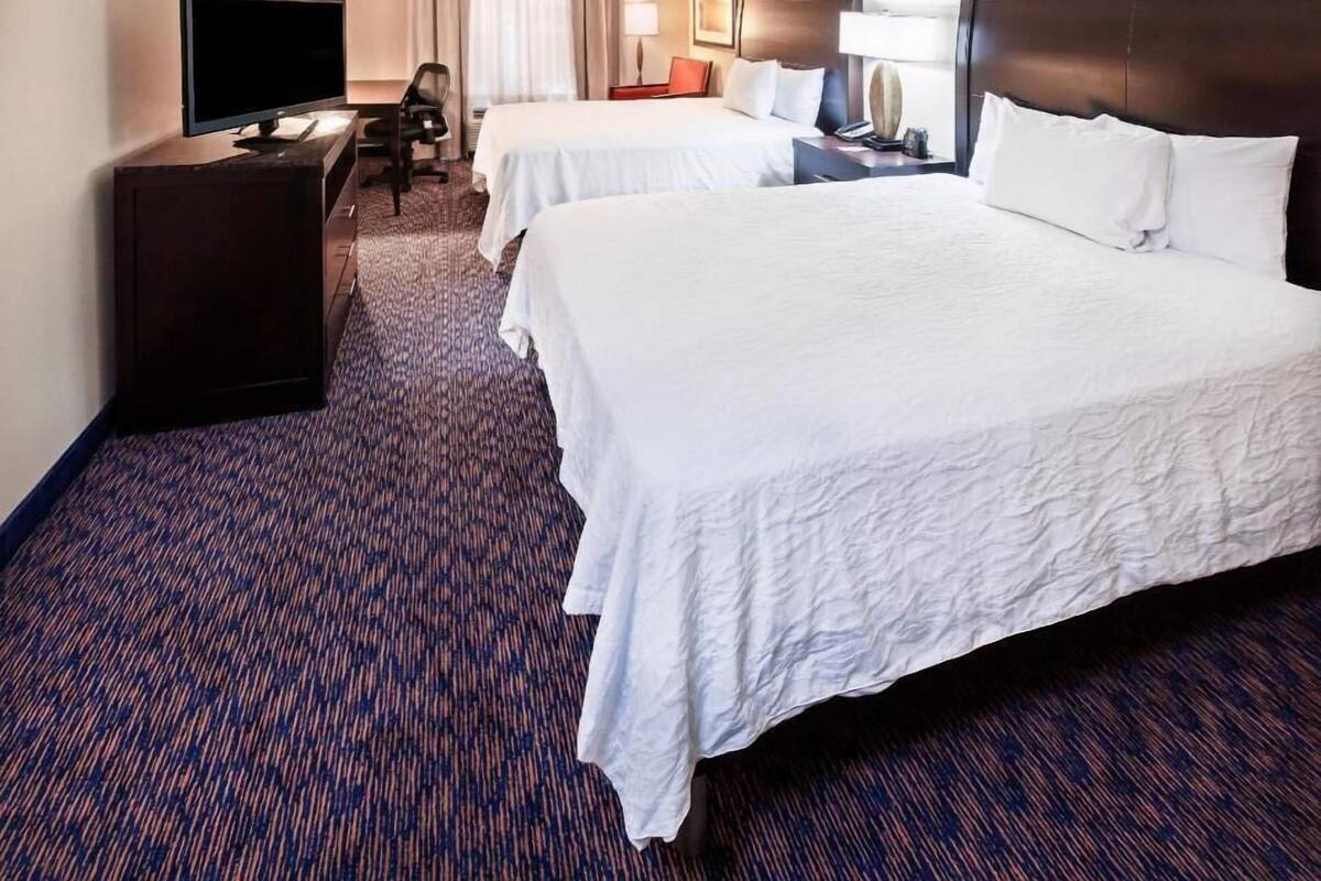 A hotel room with two beds, a TV, a desk, and a chair.