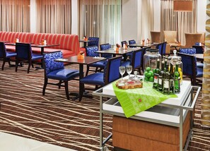 A hotel dining area with red upholstered booths, blue cushioned chairs, and tables set with wine glasses and bottles. - Hilton Garden Inn Midland (Midland)