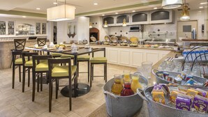 A hotel breakfast area with a buffet setup, seating arrangements, and a variety of food and drink options.