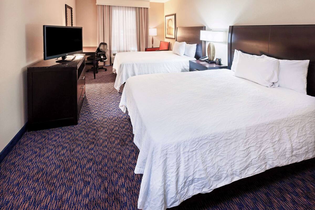 A hotel room with two beds, a desk with a computer, a TV, and a chair.