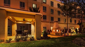 A hotel courtyard with outdoor seating, a fire pit, and a covered area with chairs and a table.