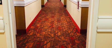 Un pasillo de hotel con alfombra estampada, paredes blancas y puertas a ambos lados.