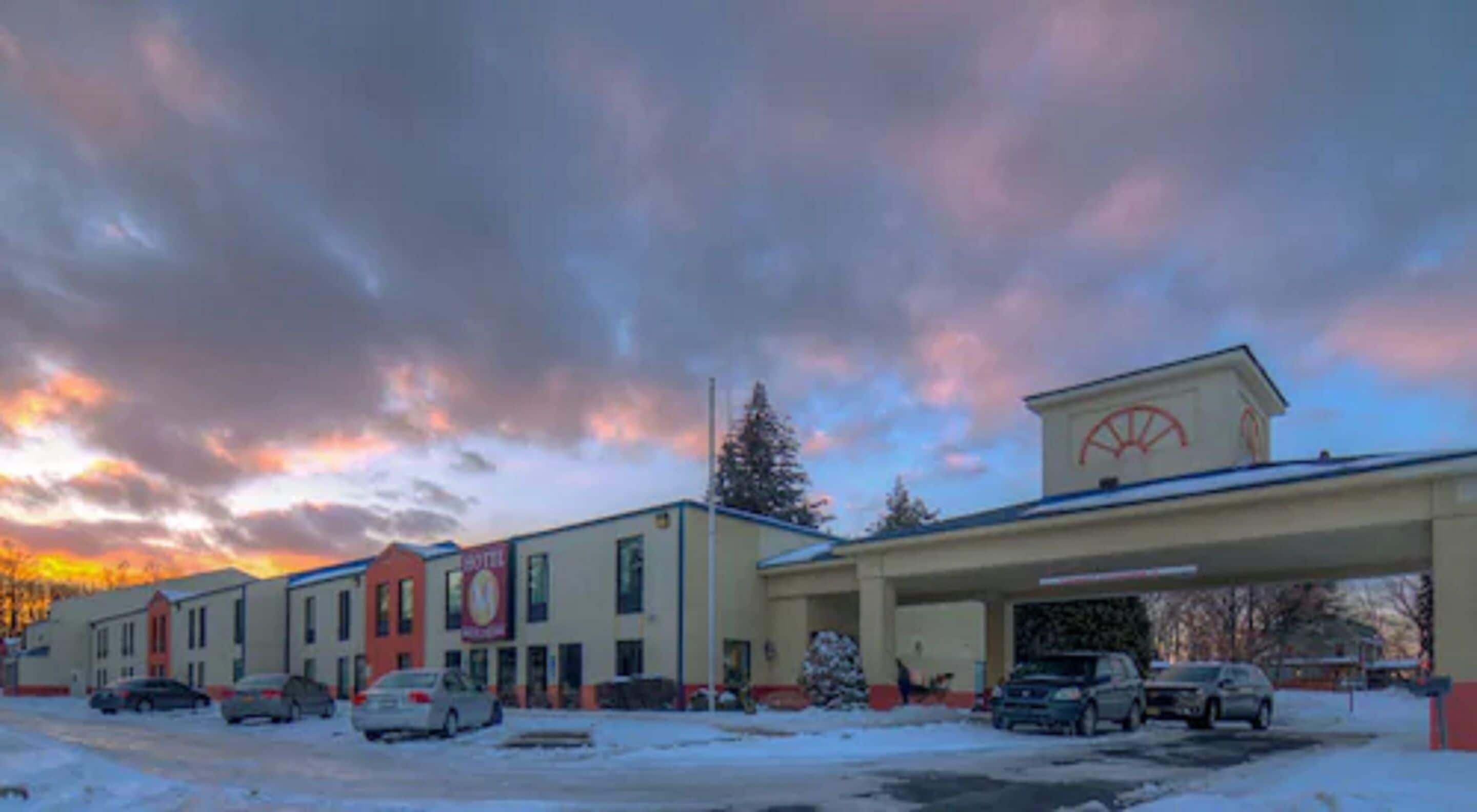 A hotel with a gas station attached, featuring a large sign with a logo, multiple parking spaces, and a snowy ground.