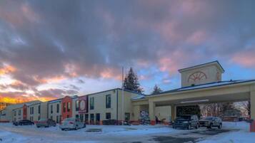 A hotel with a gas station attached, featuring a large sign with a logo, multiple parking spaces, and a snowy ground.
