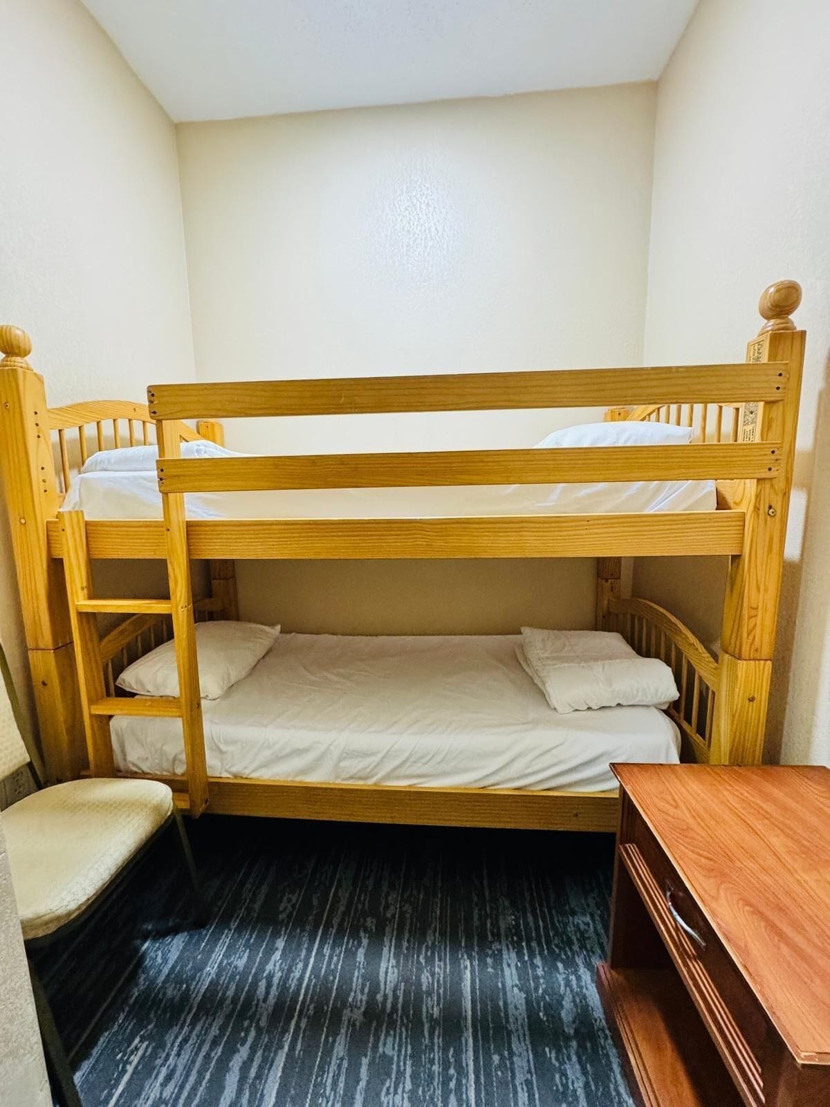 Un letto a castello con struttura in legno, una sedia e un piccolo tavolino in una stanza con pavimento scuro.