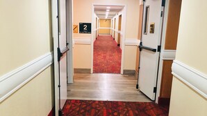 A hotel hallway with a red carpet, white walls, and doors leading to rooms.