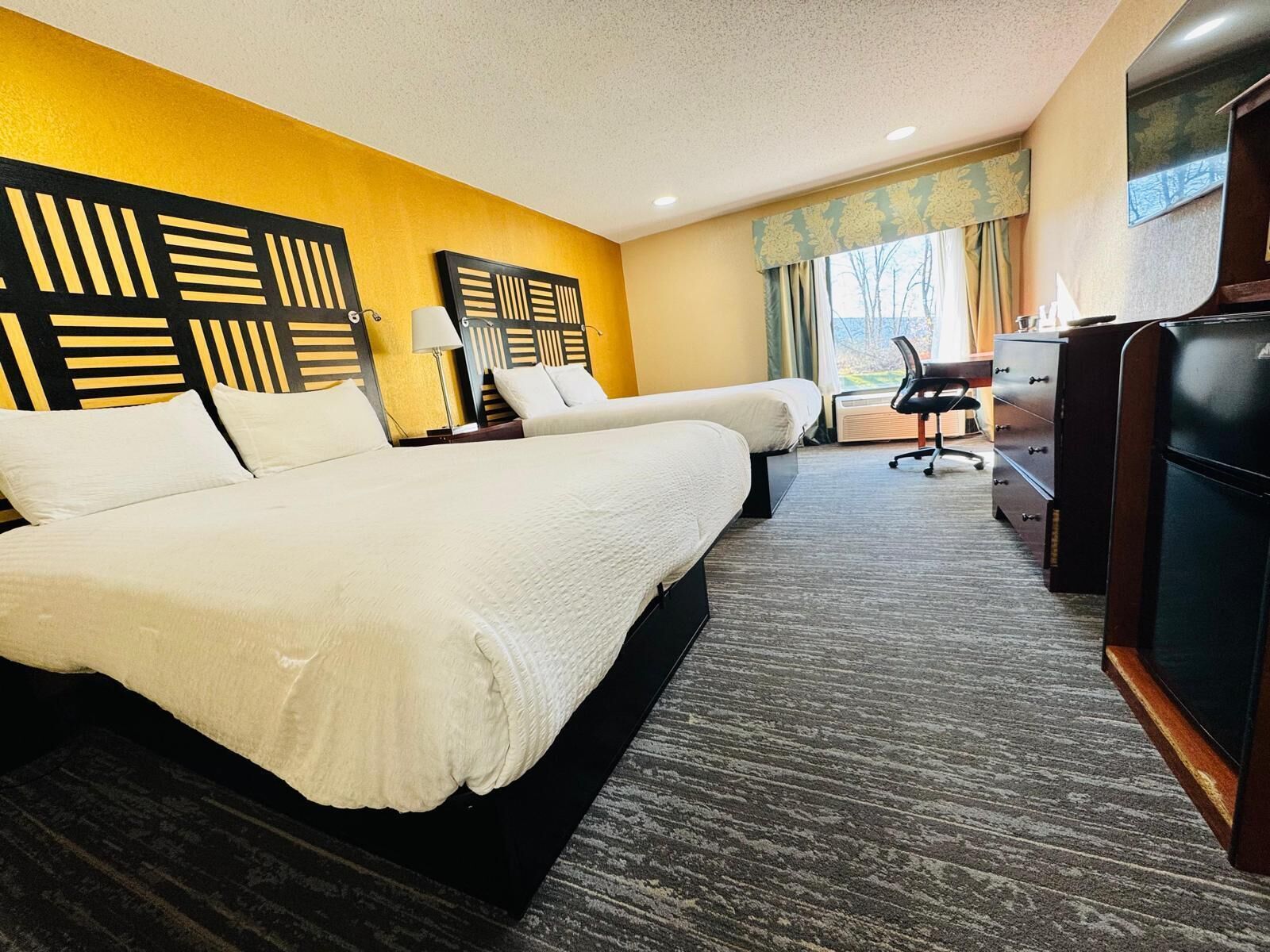 A hotel room with two beds, a desk, a chair, and a TV.