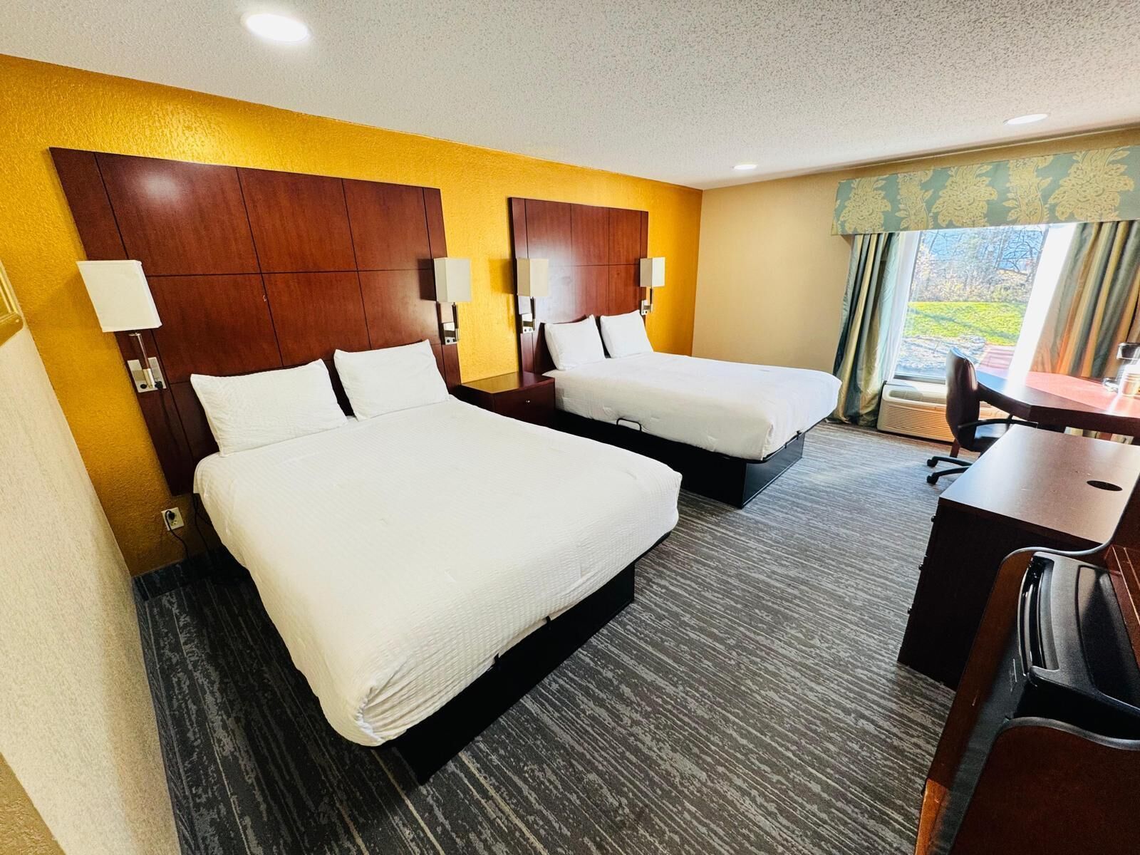 A hotel room with two beds, a desk, and a view of the outdoors.