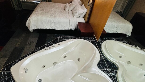 A hotel room with a large bathtub, a bed with white bedding, and a painting on the wall.