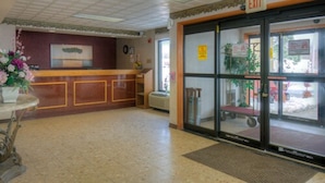 A reception area with a wooden counter, a reception desk, a large glass door with an exit sign, and a small mat at the entrance.