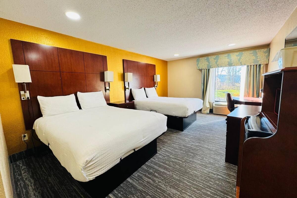 A hotel room with two beds, a desk, and a TV.