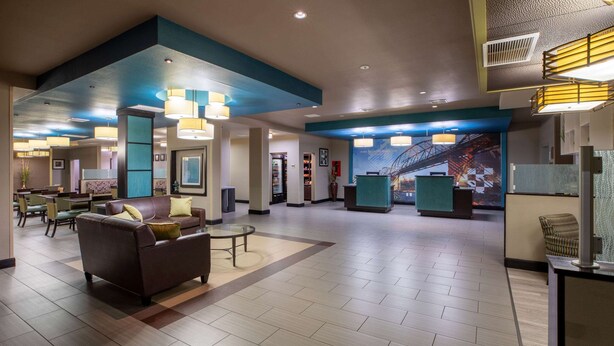 A spacious lobby with a brown sofa, a reception desk, and a large mural of a bridge. - La Quinta Inn & Suites by Wyndham Durant (Durant)