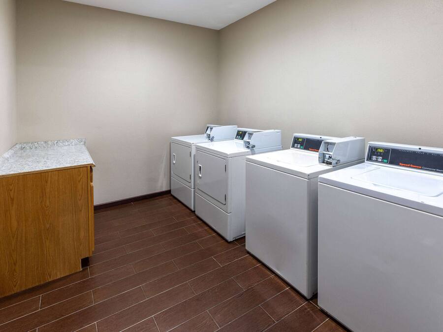A laundry room with three stacked washers and dryers, a wooden cabinet, and a tiled floor.