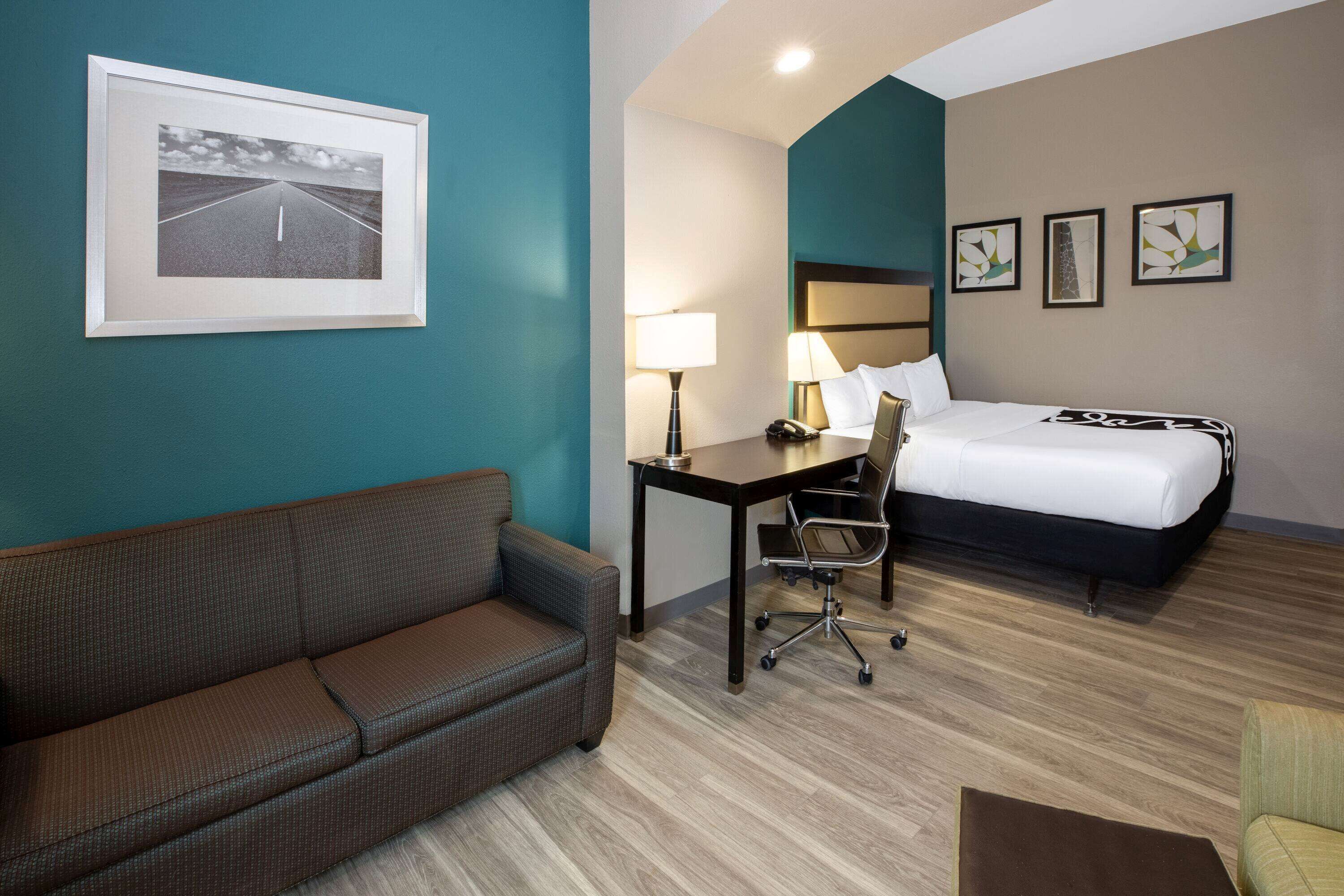 A hotel room with a bed, a desk with a chair, a sofa, and a framed picture on the wall.