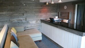 A reception area with a wooden wall, a reception desk, and a seating area with a bench and cushions. - Solé Beach (Montauk)