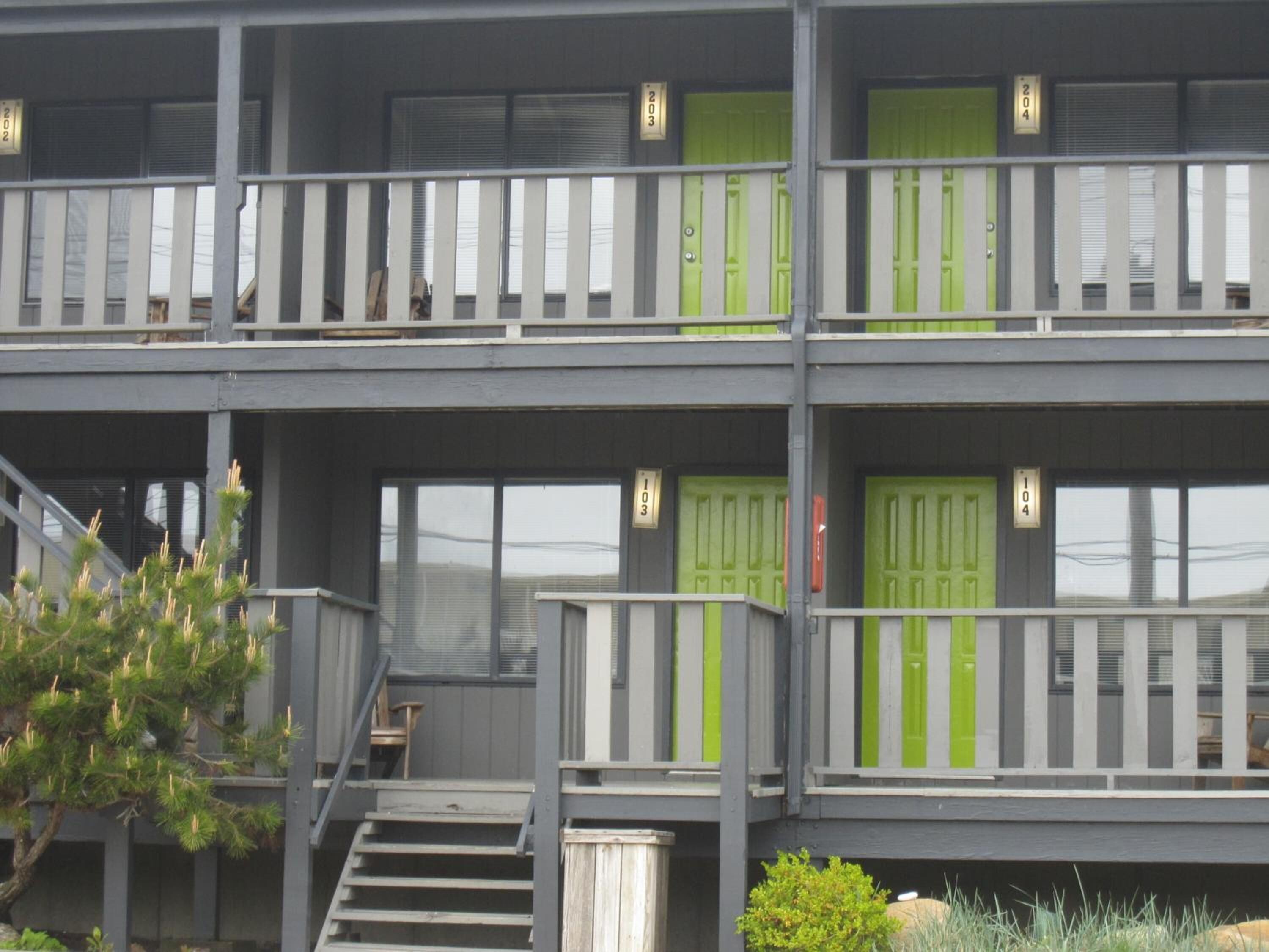 A multi-story building with balconies and green doors, featuring a staircase and a small outdoor seating area.