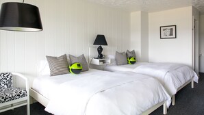 A double bed with white bedding, a black lamp on a bedside table, and a chair with patterned upholstery. - Solé Beach (Montauk)