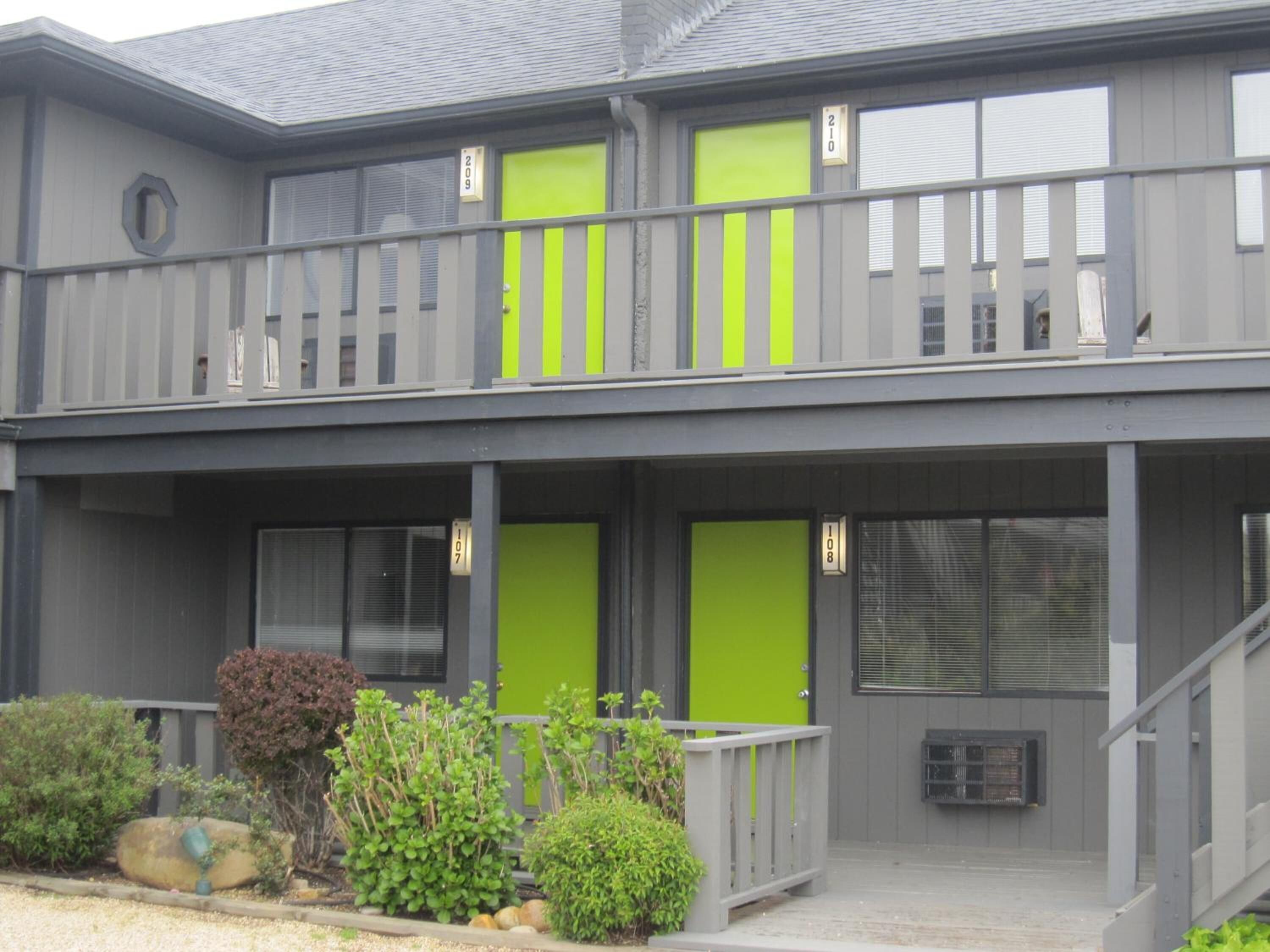 A two-story building with numbered doors, a balcony, and a small garden area.