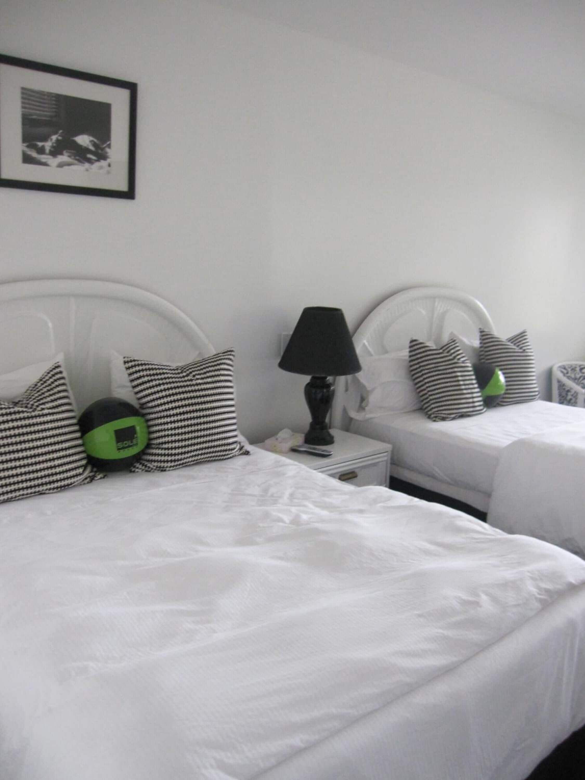 Two single beds with white headboards, a black lamp on a bedside table, and striped pillows.