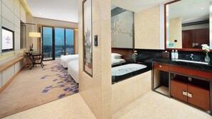 A modern hotel room with a large bed, a desk with a chair, a bathroom with a sink and mirror, and a view of the city through large windows. - Crowne Plaza Chengdu West by IHG (Chengdu)