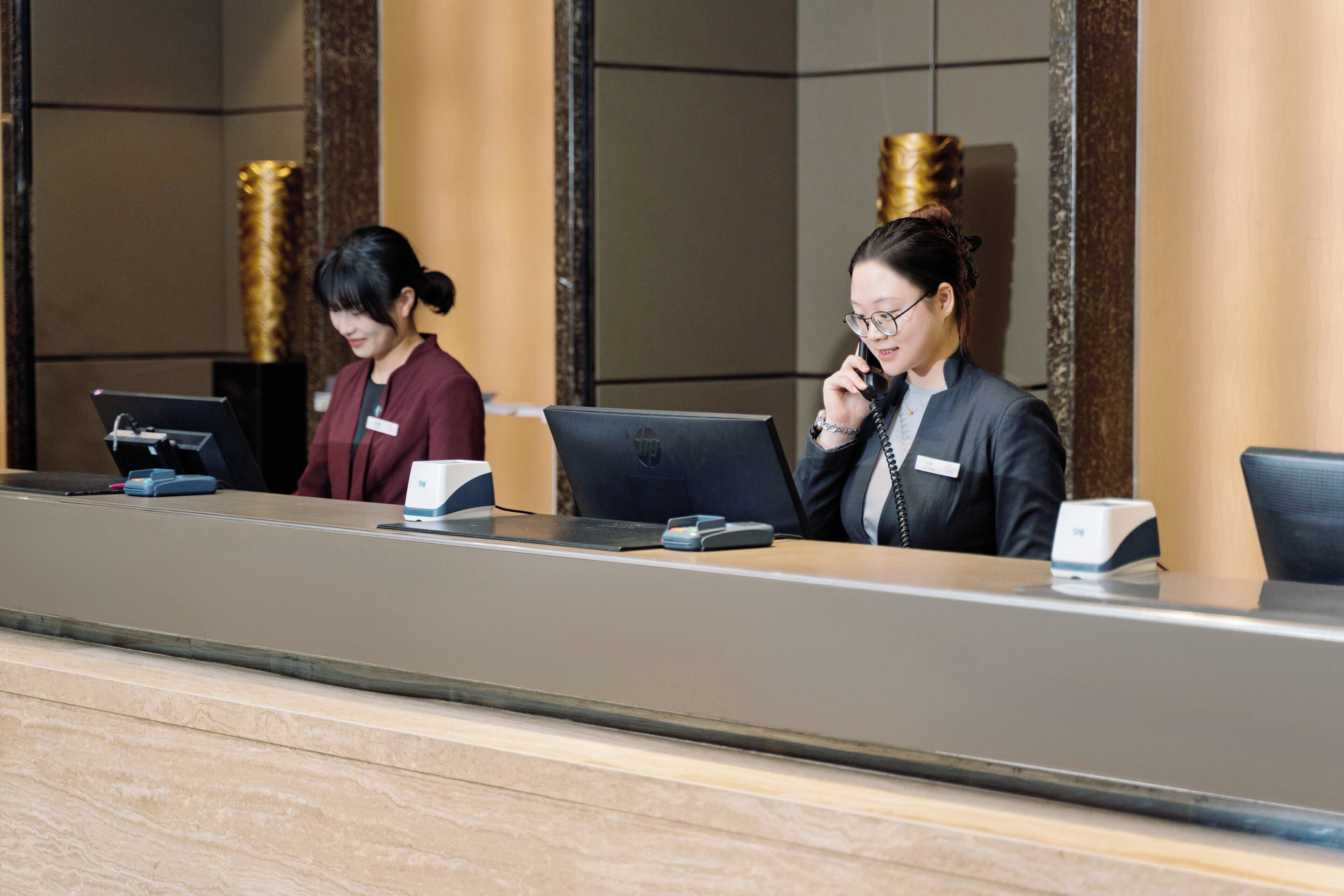 A reception desk with two staff members, a computer, and a phone.