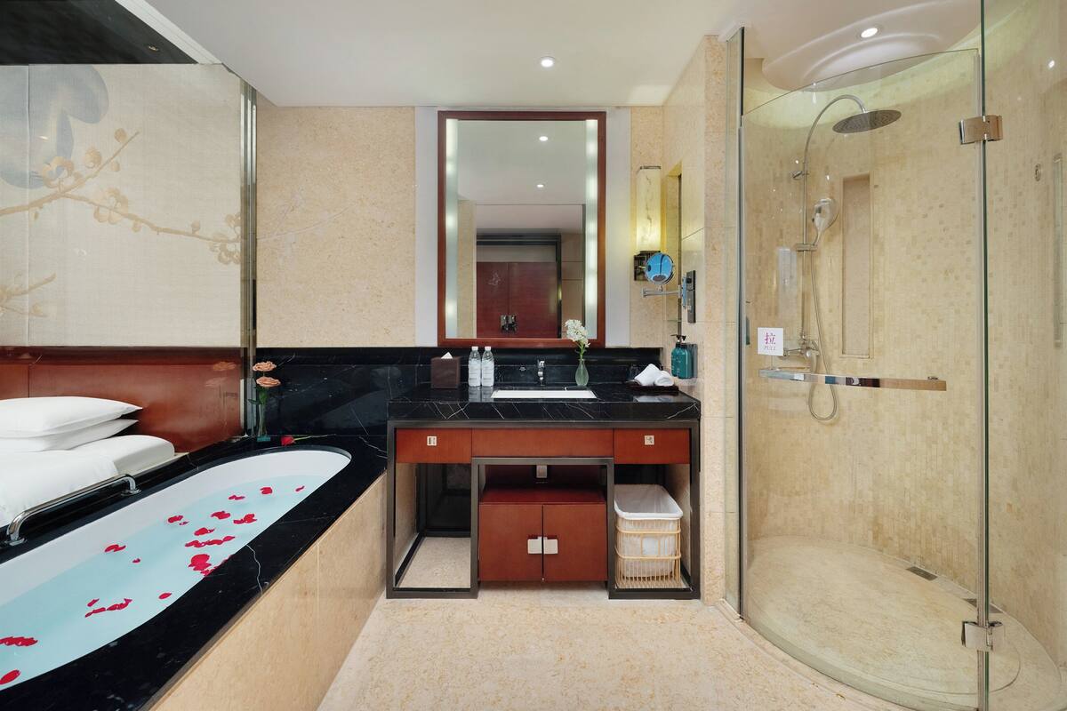 A modern bathroom with a glass-enclosed shower, a large mirror, and a black marble sink.