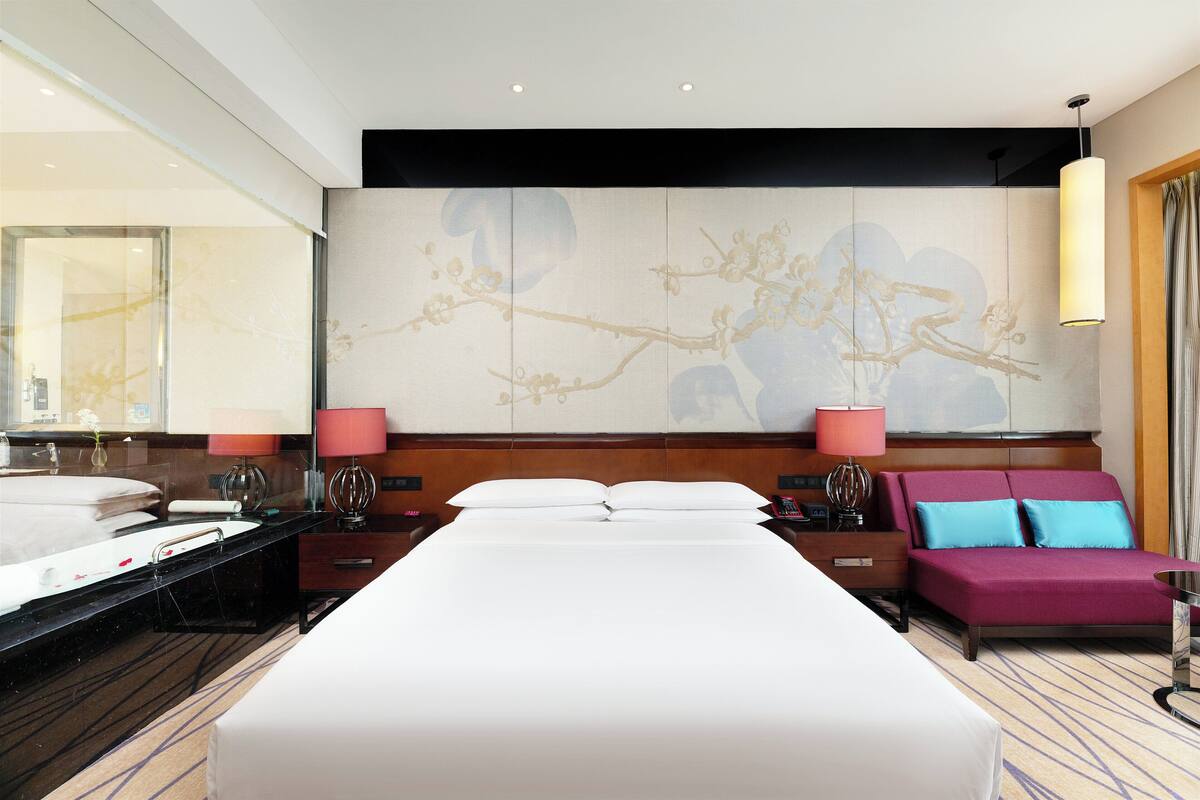 A hotel room with a large bed, a sitting area, a large mirror, and a decorative wall piece.