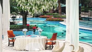 A dining area with a pool view, featuring a table set with white tablecloth, chairs, and decorative items.