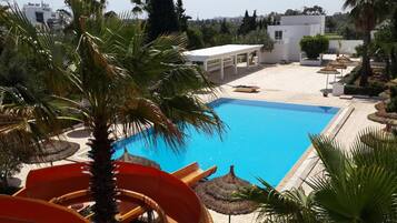 Una piscina con uno scivolo, circondata da palme e un edificio bianco.