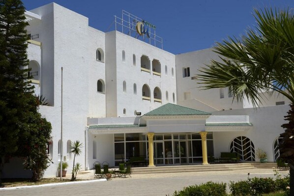 A white building with a sign reading "HOTEL" and a green roof. There are columns and a covered entrance.