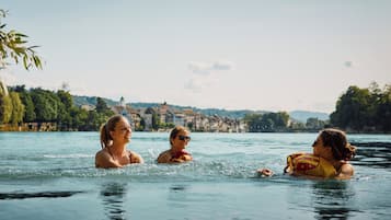 Three people in a swimming pool with a scenic view of buildings and trees in the background.