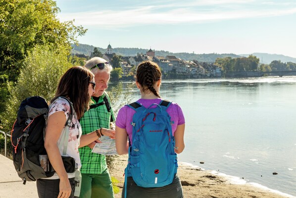 A group of people standing by a river with a town in the background. - Hotel Schützen (Rheinfelden)
