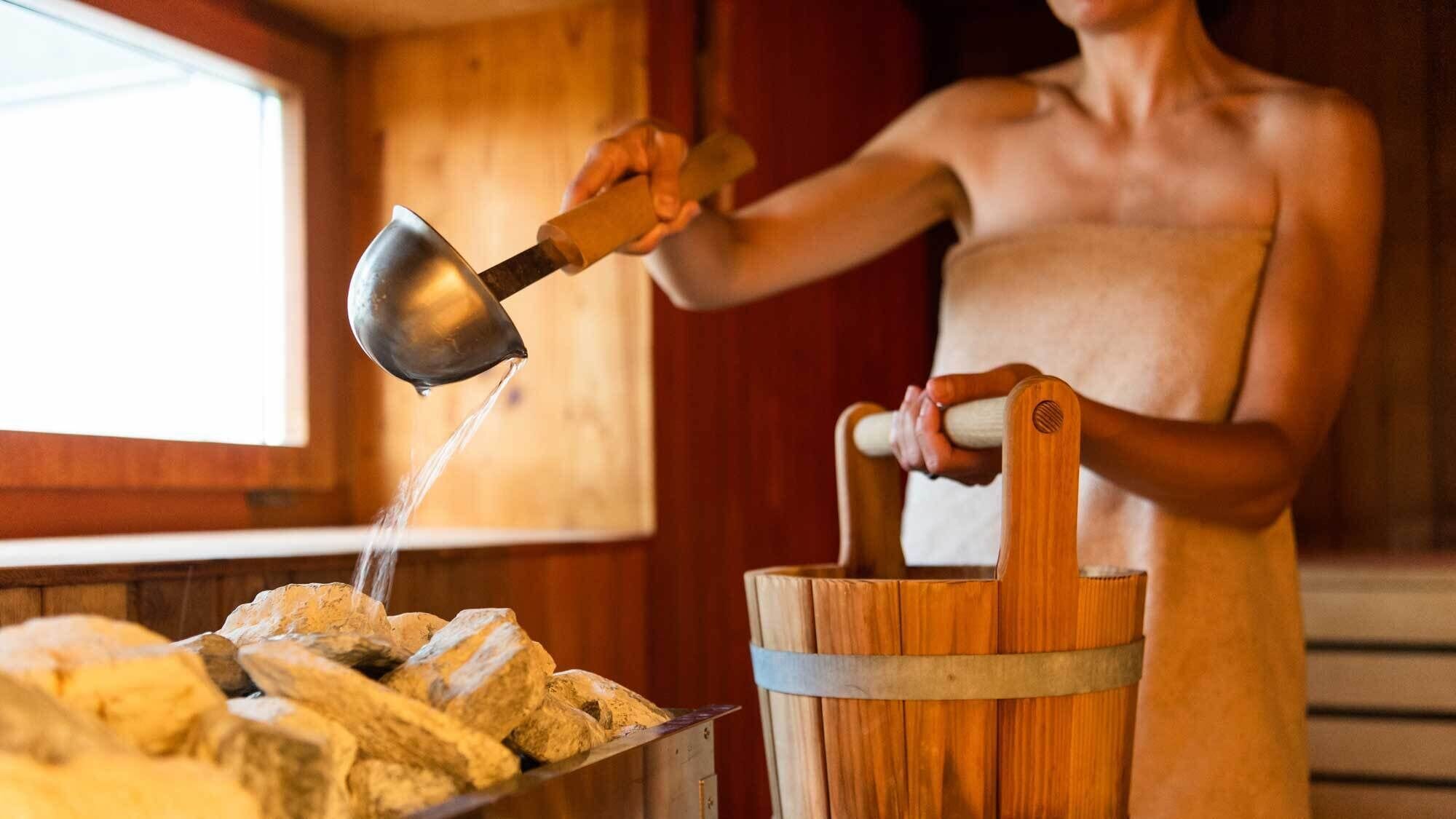 A person pouring water into a wooden trough with a metal scoop, likely for bread making.