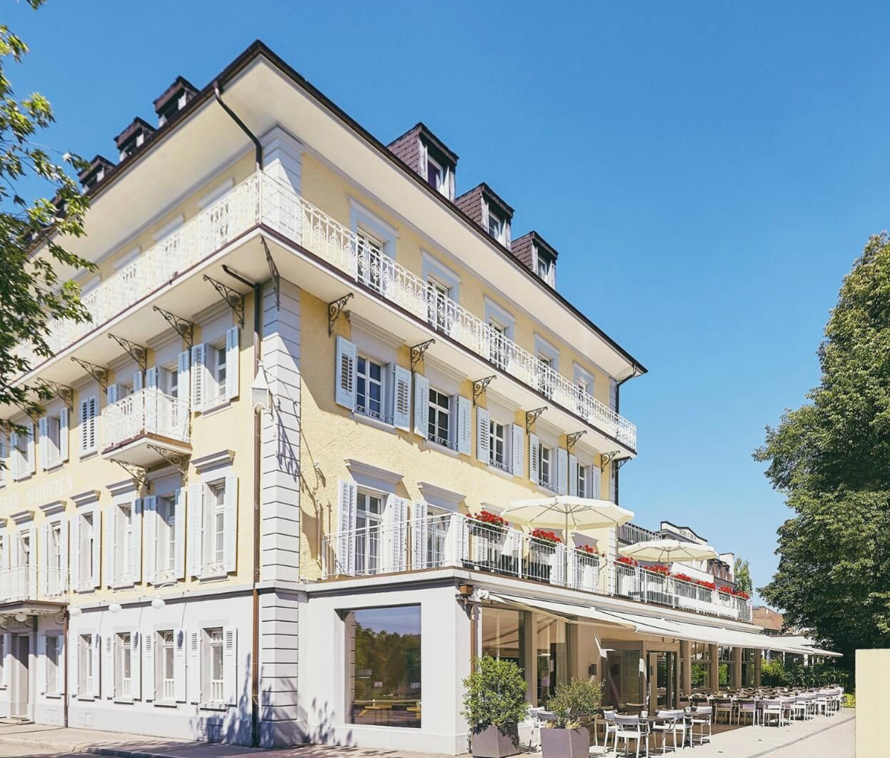 A multi-story building with balconies and outdoor seating, located in a sunny urban setting.