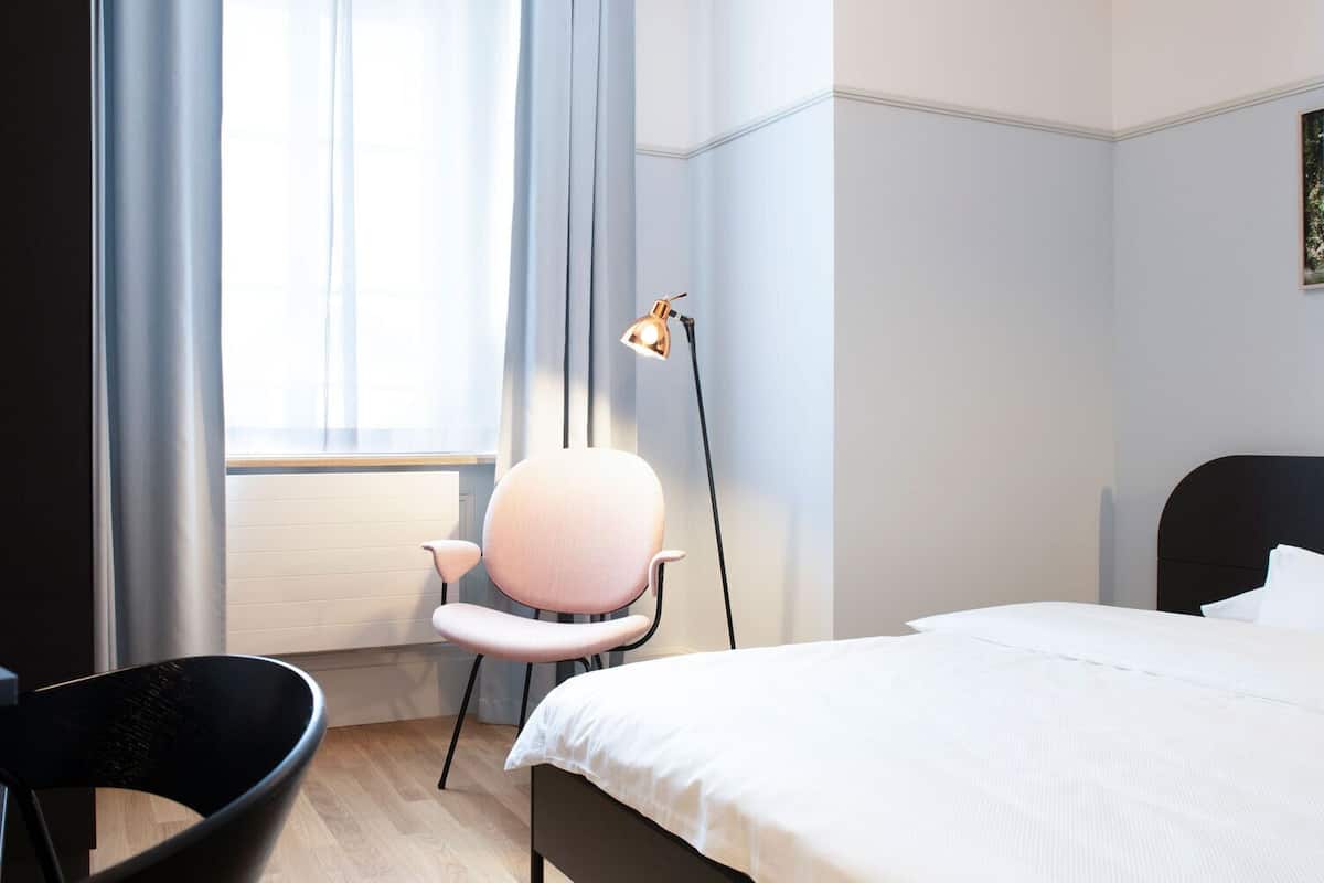 A hotel room with a bed, a desk, a chair, and a floor lamp.