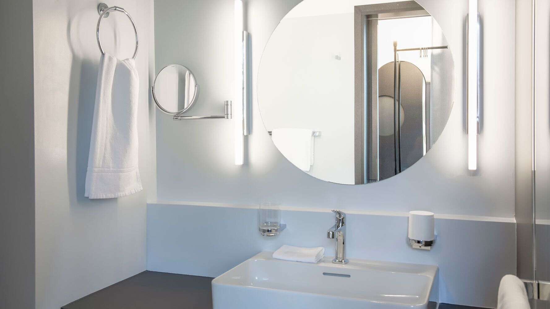 Un bagno moderno con un lavandino bianco, uno specchio rotondo e un portasciugamani.