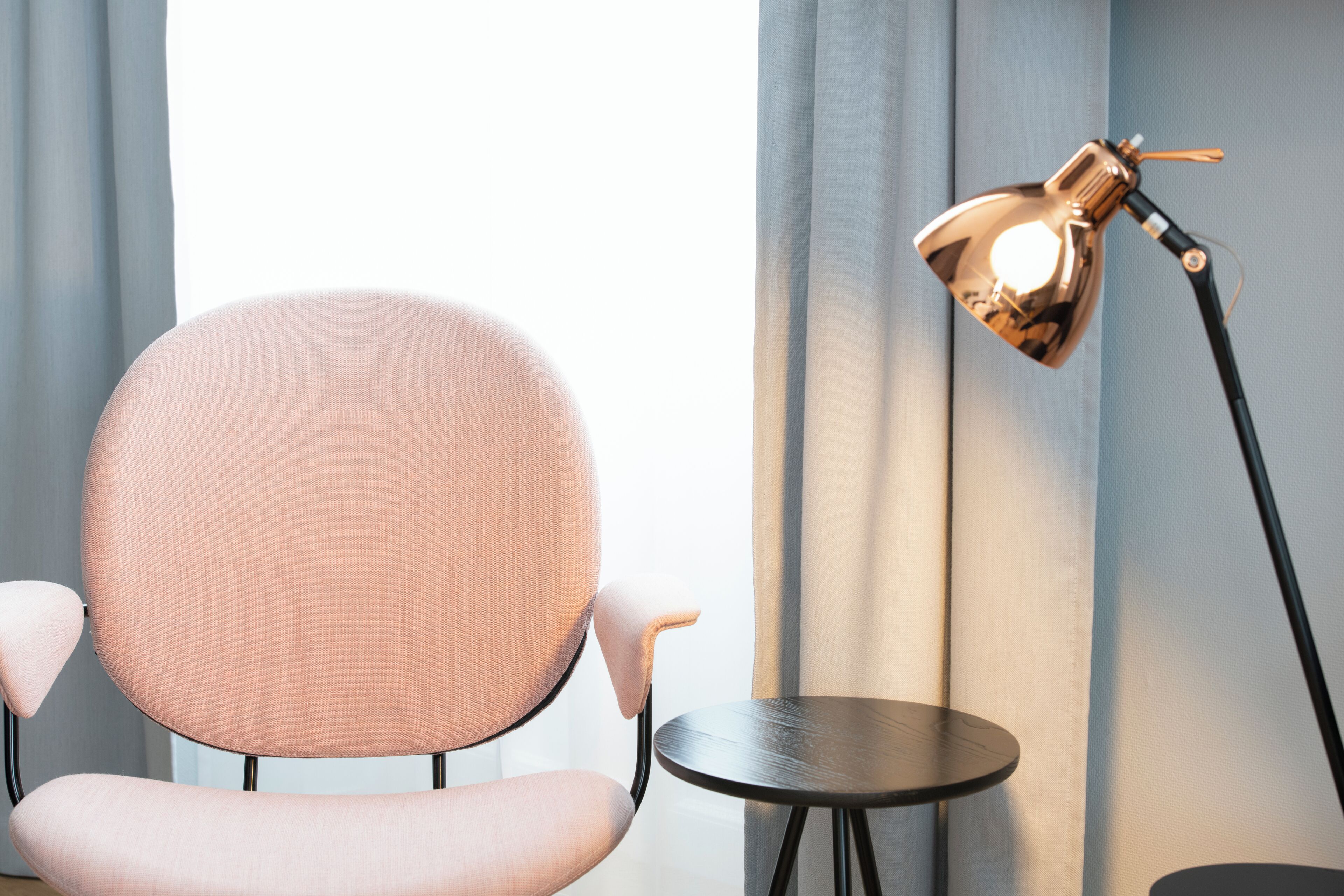 Una habitación con una silla rosa, una mesita redonda pequeña y una lámpara de pie.