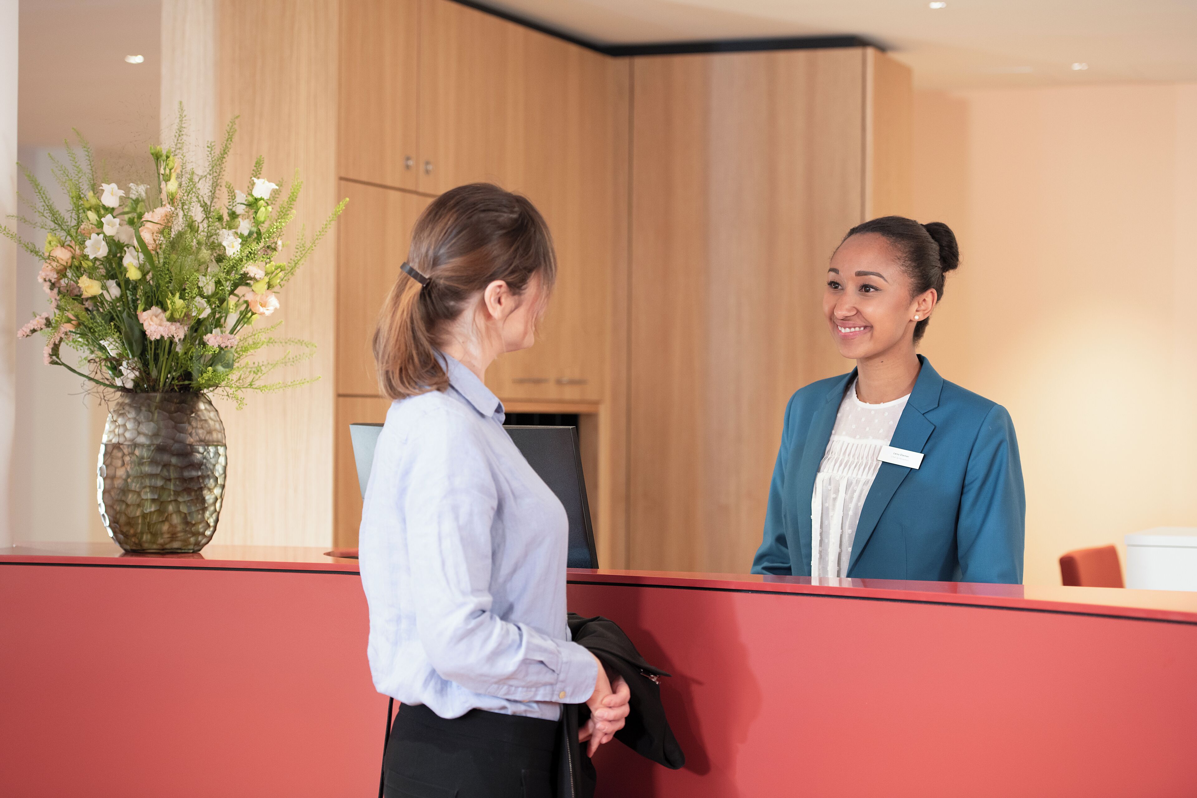A reception area with a wooden panel wall, a vase of flowers, and a red reception desk.