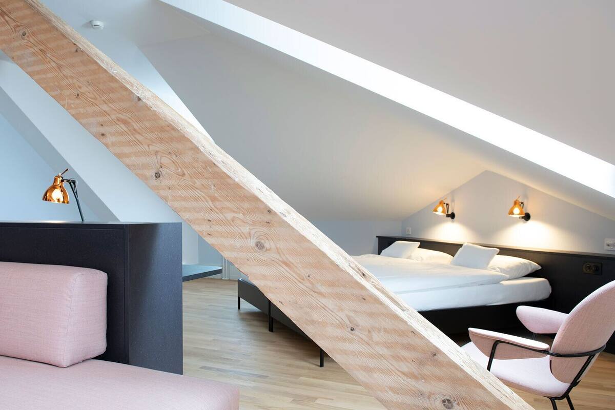 A modern loft bedroom with a sloped ceiling, a bed, a desk, and two chairs.